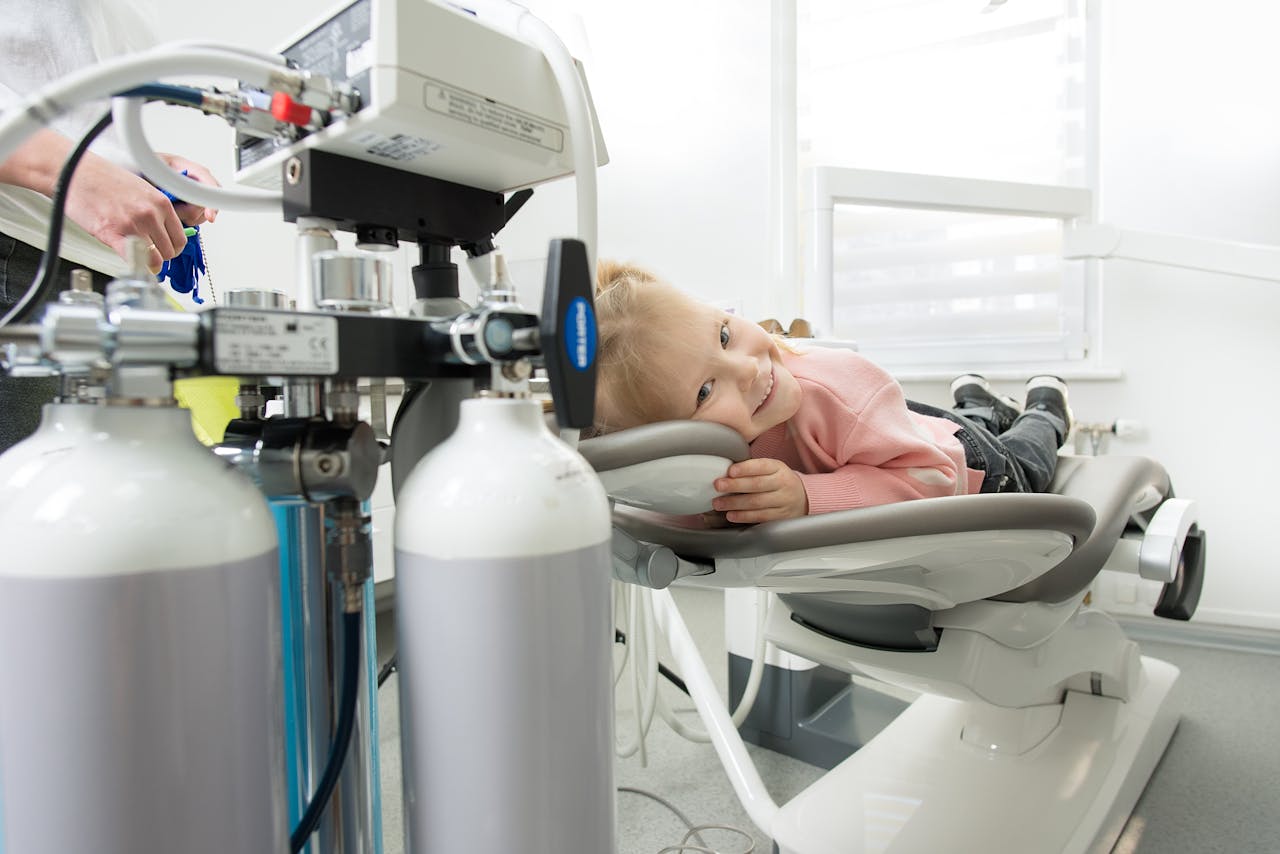 Smiling child lying on a dental chair during a checkup in a dental clinic with equipment in view.